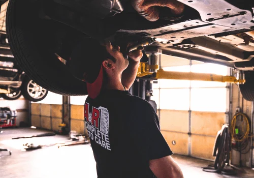 Technician performing an undercar inspection on a vehicle raised on a lift inside a professional auto repair shop.
