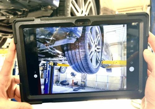 Customer viewing a digital inspection photo on a tablet showing the underside of a vehicle and tire during a transparent automotive inspection.