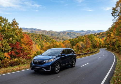 Blue Honda CR-V driving along a winding mountain road surrounded by colorful fall foliage